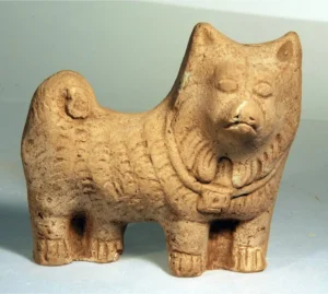 Tonfigur eines kleinen Hundes, der einen Schmuckanhänger um seinen Hals trägt, Ägypten, 2. – 3. Jh. n. Chr., Martin-von-Wagner-Museum der Universität Würzburg, © Peter Neckermann, aus: Autengruber-Thüry, Heidelinde, Hunde in der römischen Antike. Rassen-Typen-Zucht-Haltung und Verwendung, Archäopress 2021